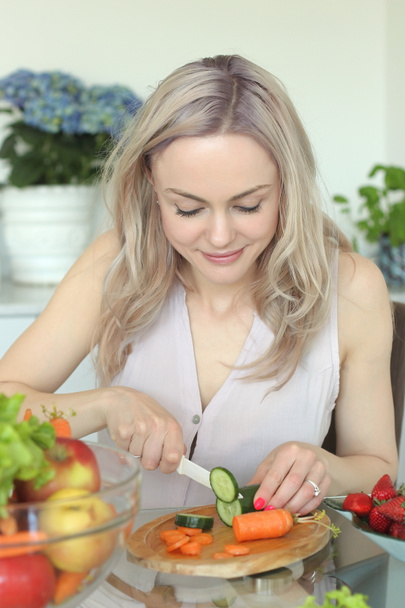 Joven mujer sonriente positiva con verduras en la cocina
 - Foto, imagen