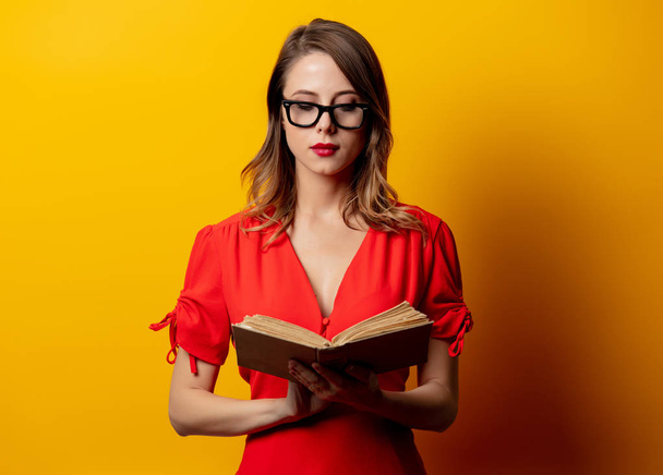 Beautiful woman in red dress with book on yellow background - Photo, Image
