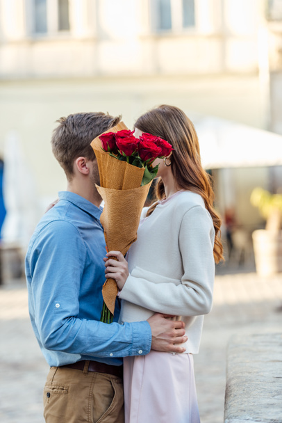 heureux couple baisers tout en se cachant derrière bouquet de roses rouges
 - Photo, image