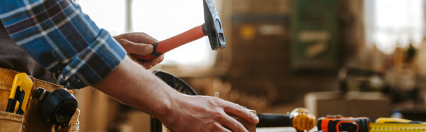panoramic shot of carpenter holding hammer in workshop  - Photo, Image