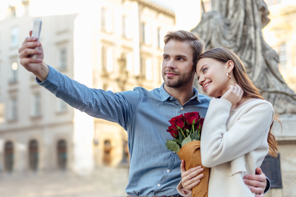 menina feliz segurando buquê de rosas enquanto namorado tomando selfie no smartphone
 - Foto, Imagem