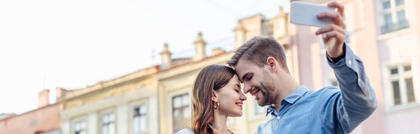 panoramic shot of happy man taking selfie with smiling girlfriend  - Photo, image
