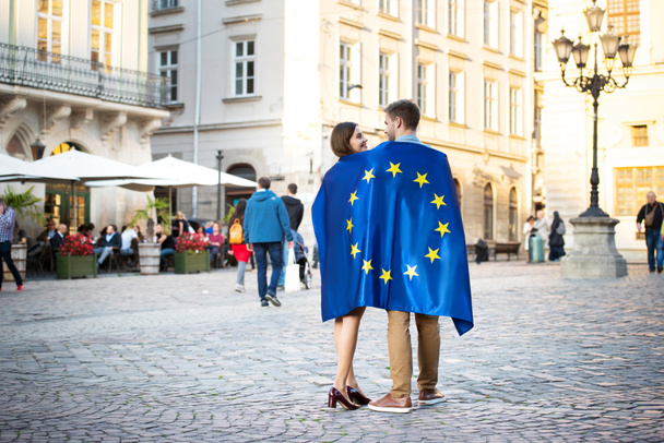 Ein paar junge Touristen, in die Fahne der Europäischen Union gehüllt, stehen auf dem Stadtplatz - Foto, Bild