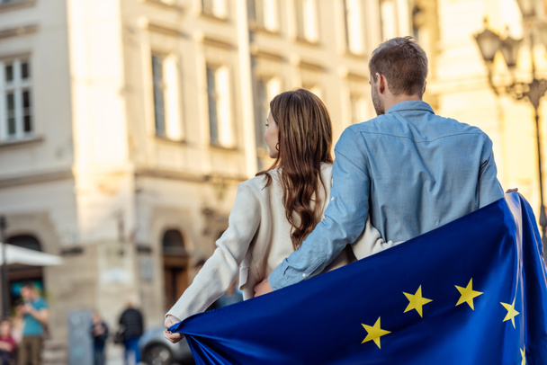 vista trasera de la pareja joven, envuelta en la bandera de la unión europea, de pie en la calle
 - Foto, Imagen