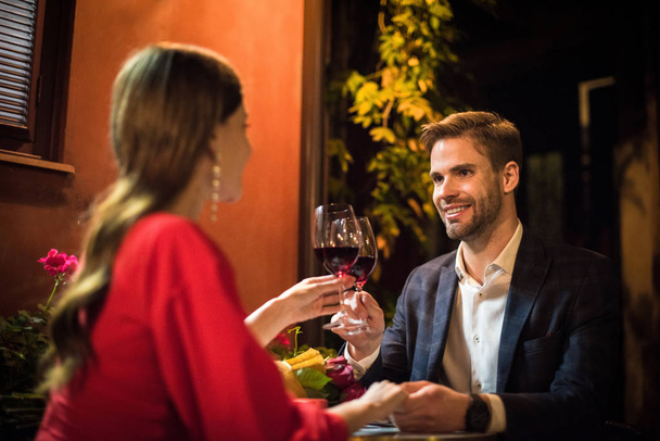 ευτυχισμένος άνθρωπος clinking ποτήρια του κόκκινου κρασιού με τη φίλη, ενώ κάνοντας πρόταση γάμου - Φωτογραφία, εικόνα