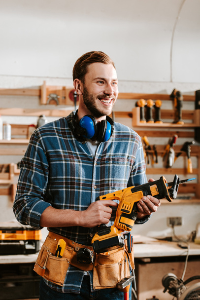 cheerful bearded carpenter holding hammer drill  - Fotoğraf, Görsel