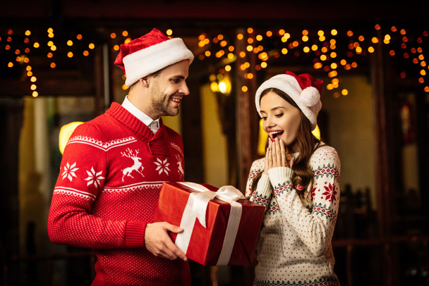 smiling man presenting christmas gift to amazed girlfriend  - Foto, Bild