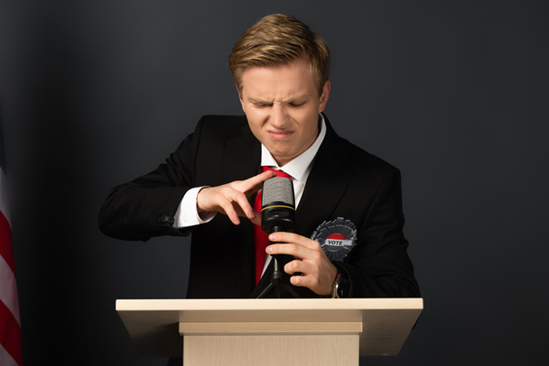 emotionele man aanraken microfoon op tribune op zwarte achtergrond - Foto, afbeelding