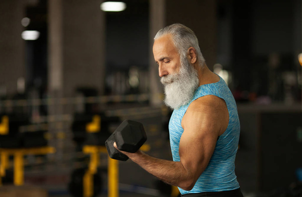 Senior-Mann in Sportkleidung trainiert im Fitnessstudio mit Gewichten. - Foto, Bild