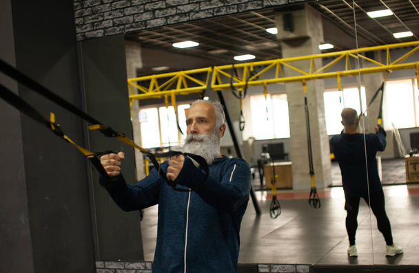 Bearded senior sportsman training with trx resistance bands in gym. - Photo, Image