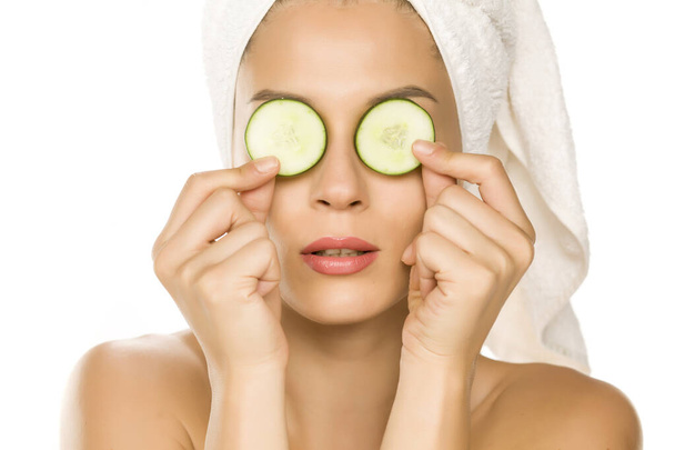 Young woman posing with slices of cucumbers on her eyes on white background - Фото, зображення