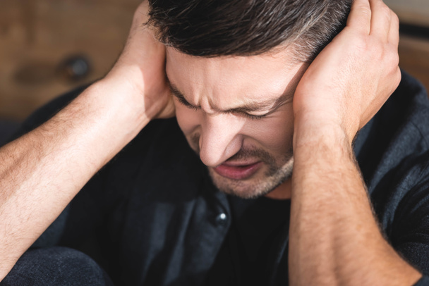 handsome man in black shirt with headache touching head in apartment  - Foto, immagini