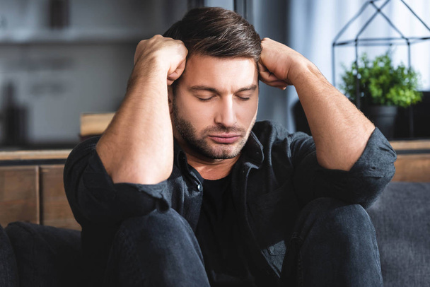 handsome man in black shirt with headache touching head in apartment  - Foto, Imagem