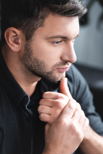 handsome and pensive man in black shirt looking away in apartment  - 写真・画像
