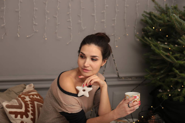 Kaunis nuori tyttö lämpimässä puserossa piparkakkukeksien ja kupin teetä kanssa
 - Valokuva, kuva