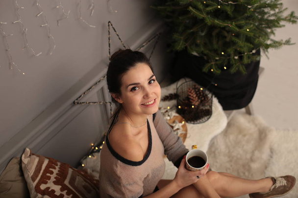 Kaunis nuori tyttö lämpimässä puserossa piparkakkukeksien ja kupin teetä kanssa
 - Valokuva, kuva