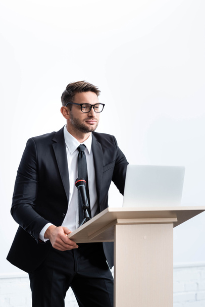 puvussa oleva liikemies seisoo puhujakorokkeella ja katselee poispäin konferenssissa, joka on eristetty valkoisella
 - Valokuva, kuva