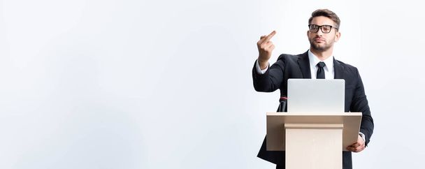 plano panorámico de hombre de negocios en traje de pie en el podio tribuna y mostrando el dedo medio durante la conferencia aislado en blanco
 - Foto, Imagen