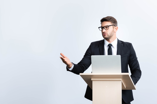 puvussa oleva liikemies seisoo puhujakorokkeella ja puhuu konferenssissa valkoisella eristyksissä
 - Valokuva, kuva