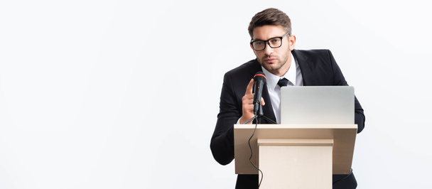 tiro panorâmico de empresário de terno em pé no tribuno pódio e falando durante conferência isolada em branco
  - Foto, Imagem