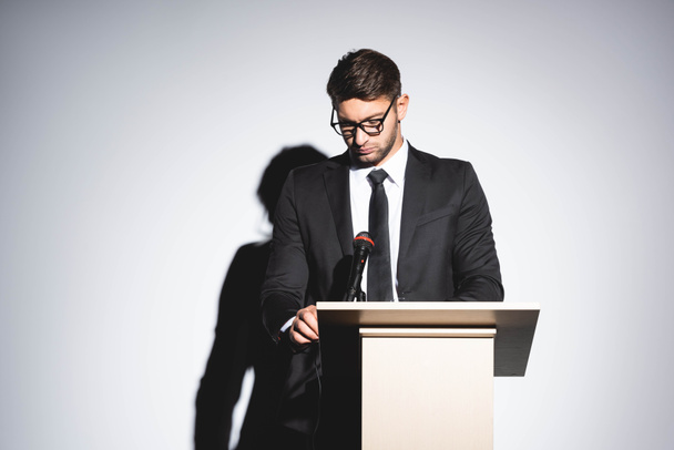 pukuinen liikemies seisoo puhujakorokkeella ja katselee alas konferenssin aikana valkoisella taustalla
  - Valokuva, kuva