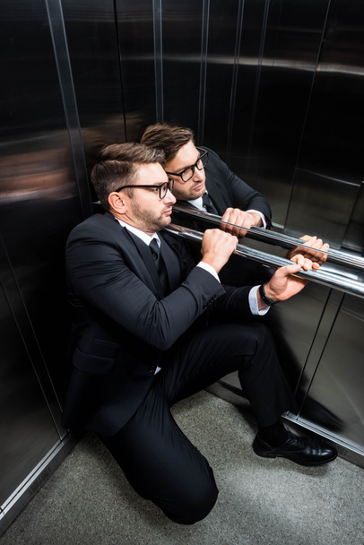 high angle view of scared businessman in suit with claustrophobia sitting on floor in elevator - Photo, Image