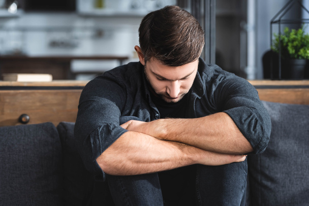 handsome and sad man in shirt hugging legs in apartment  - Photo, image