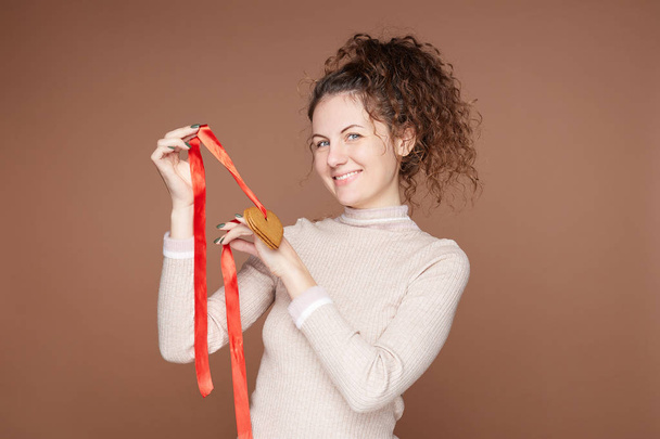 Kędzierzawe europejskie kobieta demonstruje do kamery ręcznie świeże ciasteczka imbirowe w kształcie serca, będzie ozdobić miejsce na Boże Narodzenie i Nowy Rok, ma doskonały manicure, łagodny uśmiech. - Zdjęcie, obraz