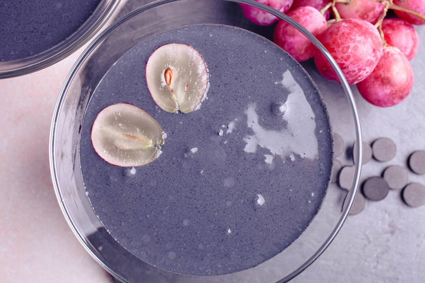 Yogur negro con carbón activado y uvas rojas sobre fondo blanco
. - Foto, imagen