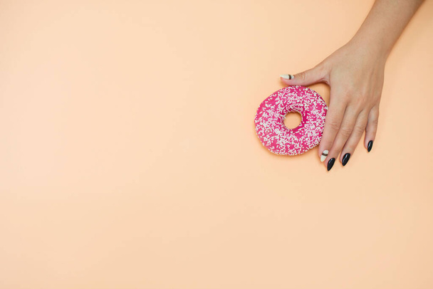Appetizing donuts with icing on a colored background with female hands with a beautiful manicure. - Fotoğraf, Görsel