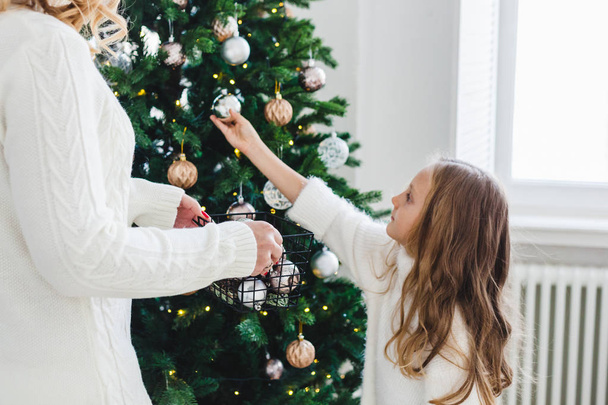 A girl with her mother decorate the Christmas tree, the interior is decorated for the new year and Christmas, family and joy, traditions. - Foto, Imagen