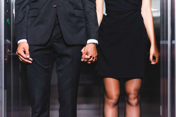 Cropped view of business couple holding hands in office elevator  - Photo, Image