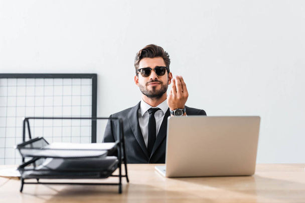 Handsome businessman in sunglasses gesturing at office table  - Foto, Imagen