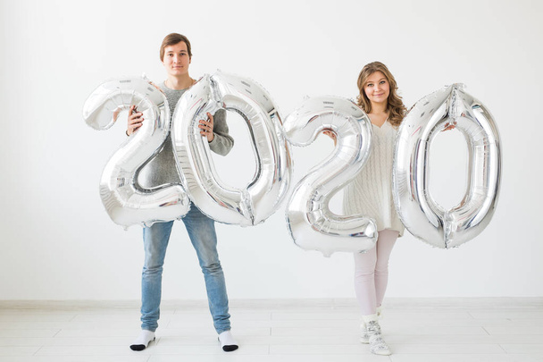 Holidays, festive and party concept - Happy loving couple kisses and holds silver 2020 balloons on white background. New Year celebration - Fotó, kép