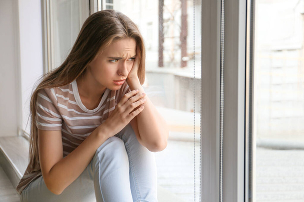 Depressed woman near window at home - 写真・画像
