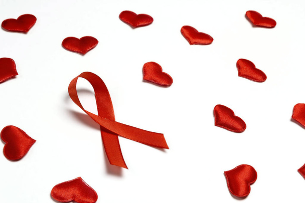 Red ribbon as symbol of aids awareness with red hearts on white  - Photo, Image