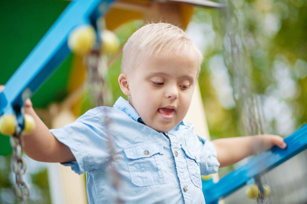 Codzienne życie dziecka niepełnosprawnego. Chłopiec z zespołem Downa bawi się na placu zabaw. Zaburzenia chromosomowe i genetyczne u dziecka. - Zdjęcie, obraz