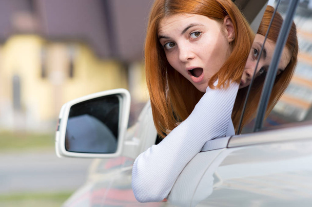 Νεαρή γυναίκα οδηγεί ένα αυτοκίνητο ανάποδα. Κορίτσι με αστεία έκφραση  - Φωτογραφία, εικόνα