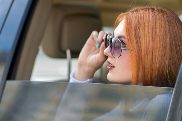 車で旅行する赤い髪とサングラスを持つ若い女性。パス - 写真・画像
