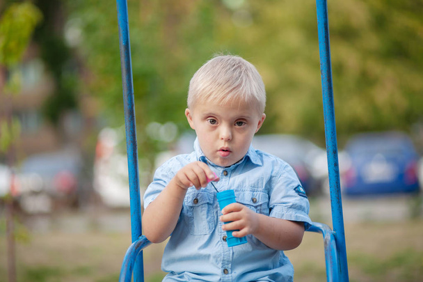 La vida cotidiana de un niño con discapacidad. Un niño con síndrome de Down está jugando en el patio de recreo. Trastorno cromosómico y genético en el bebé
. - Foto, Imagen