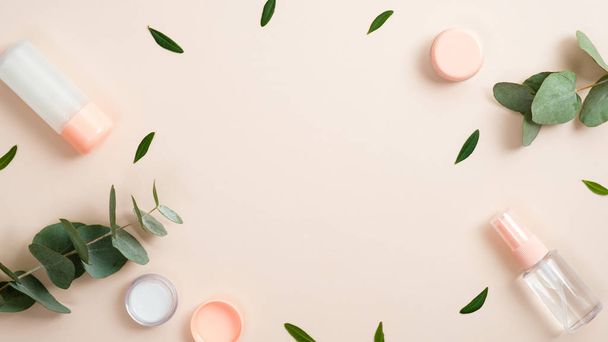 Frame made of natural organic cosmetic bottle containers with green herbal leaves on pastel beige background. Natural beauty product concept. Banner mockup for beauty blog. Flat lay, top view. - 写真・画像