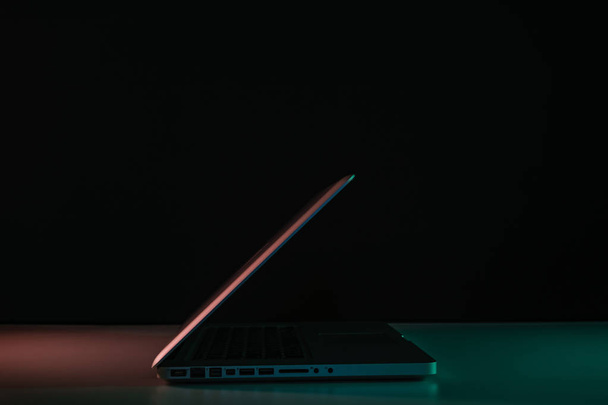 Серебристый ноутбук в цветном свете на столе и ночном фоне
. - Фото, изображение