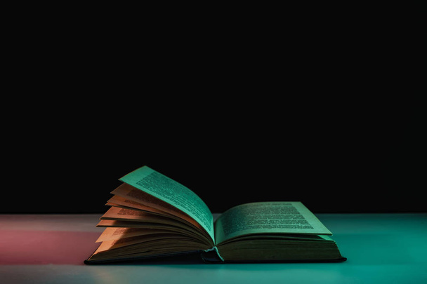 Gyönyörű nyitott könyv a színes fény az asztalon és az éjszakai háttér. - Fotó, kép