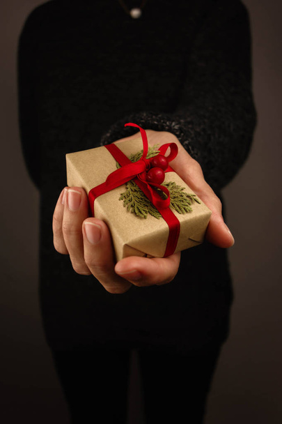 Elinde küçük bir Noel hediyesi tutan koyu renk kazaklı bir kadın. Siyah arkaplan. - Fotoğraf, Görsel