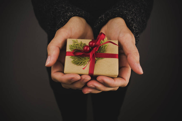 Жінка з темним светром тримає маленький різдвяний подарунок. Чорний фон
. - Фото, зображення