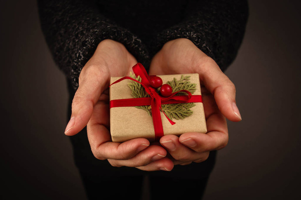 Mulher com camisola escura segurando um pequeno presente de Natal. Fundo preto
. - Foto, Imagem