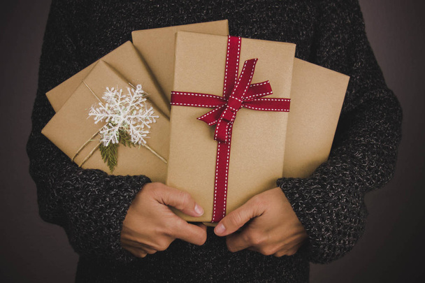 Woman with dark sweater holding many Christmas presents. Black background. - Photo, Image