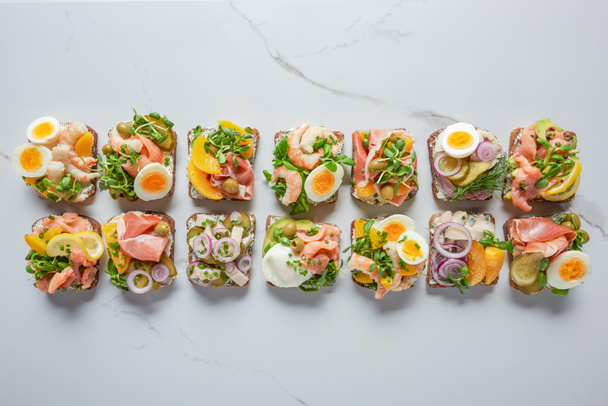 vrchní pohled na vynikající dánské smorrebrod sendviče na bílém mramorovém povrchu  - Fotografie, Obrázek