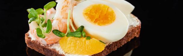 panoramic shot of rye bread with delicious shrimp near egg on smorrebrod sandwich on black  - Photo, Image