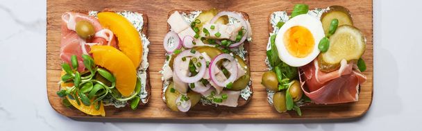 Beyaz mermer yüzeyde lezzetli smorrebrod sandviçlerle ahşap kesim tahtasının panoramik görüntüsü.  - Fotoğraf, Görsel